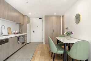 A modern kitchen with a dining area, featuring a white countertop, stainless steel appliances, and light wood cabinetry. - Elegant Urban Retreat in the Heart of Epping (Epping)