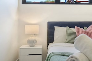 A neatly made bed with a dark headboard, a bedside lamp, and a white nightstand with a drawer. - Elegant Urban Retreat in the Heart of Epping (Epping)