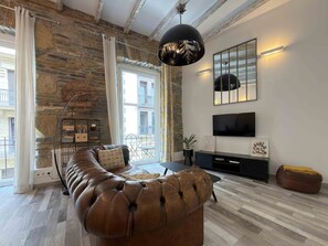 Un salon moderne avec un mur en pierre, un canapé en cuir, un téléviseur et une grande fenêtre.