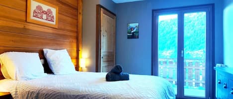A bedroom with a bed, a wooden headboard, a door, a wall-mounted picture, and a view through a glass door.