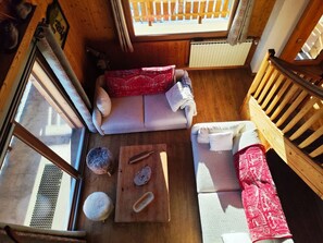 A cozy room with a wooden floor, a sofa, a small table with a cutting board, and a window with a view of a wooden deck. - Le Montagnard (8 people) View of Mont Blanc & covered parking (Saint-Gervais-les-Bains)