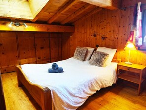 Habitació de fusta amb un llit, una tauleta de nit i una làmpada.