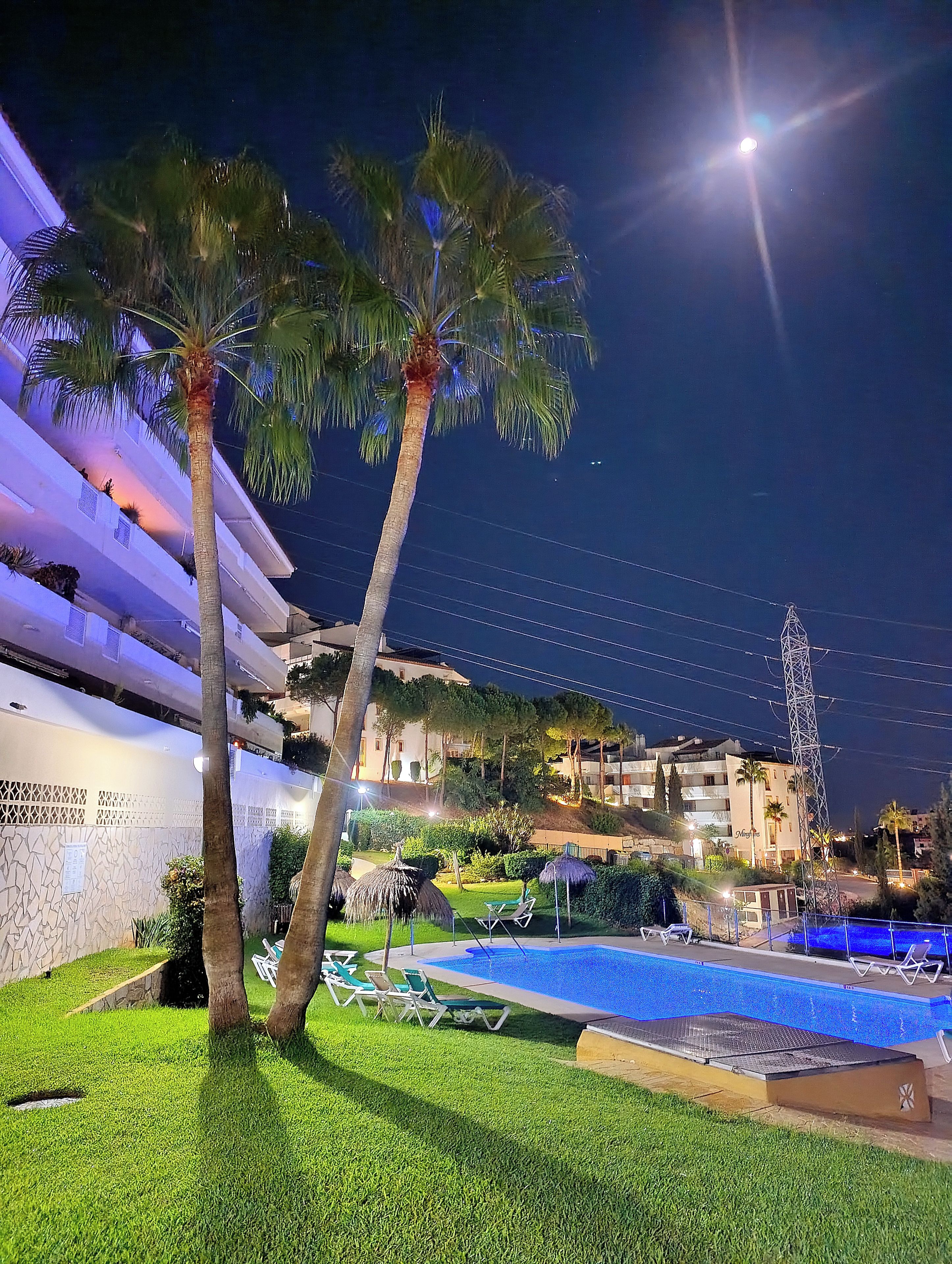 Ein Nachtblick auf ein Hotel mit Schwimmbad, Palmen und einer gut beleuchteten Fassade.