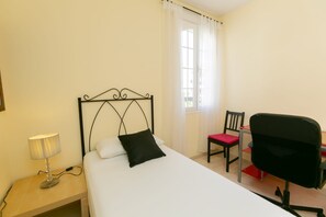 Et hotelværelse med seng, skrivebord, stol og lampe.