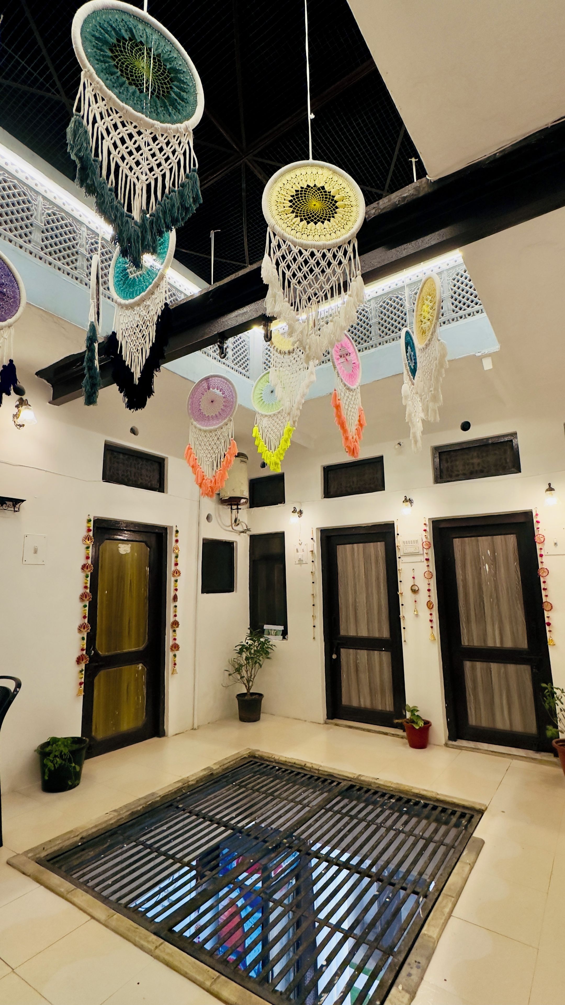 Una habitación con un espacio central abierto, macramé decorativo colgando del techo y una planta en maceta sobre el suelo.