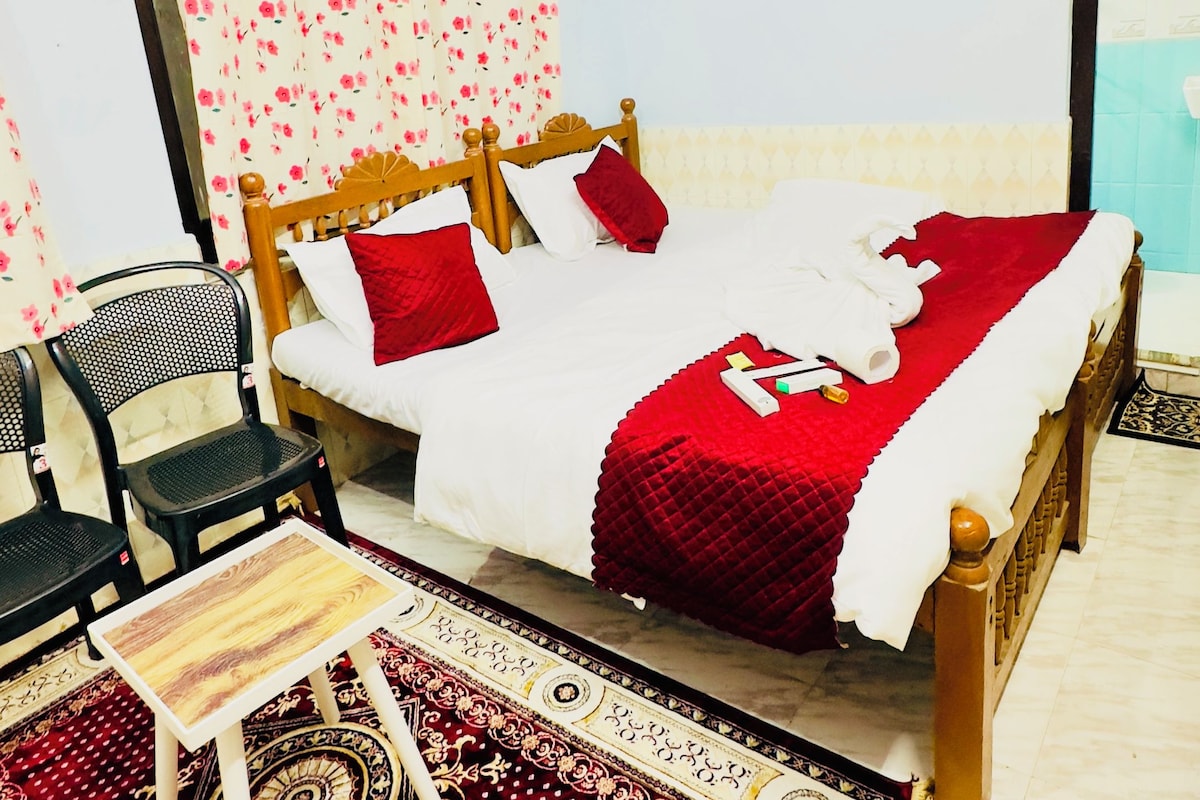 A room with a bed, a chair, a small table, and a patterned rug.