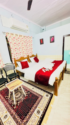 A room with a bed, a chair, a small table, and a patterned rug. - Hotel Hermosa Pushkar (Pushkar)