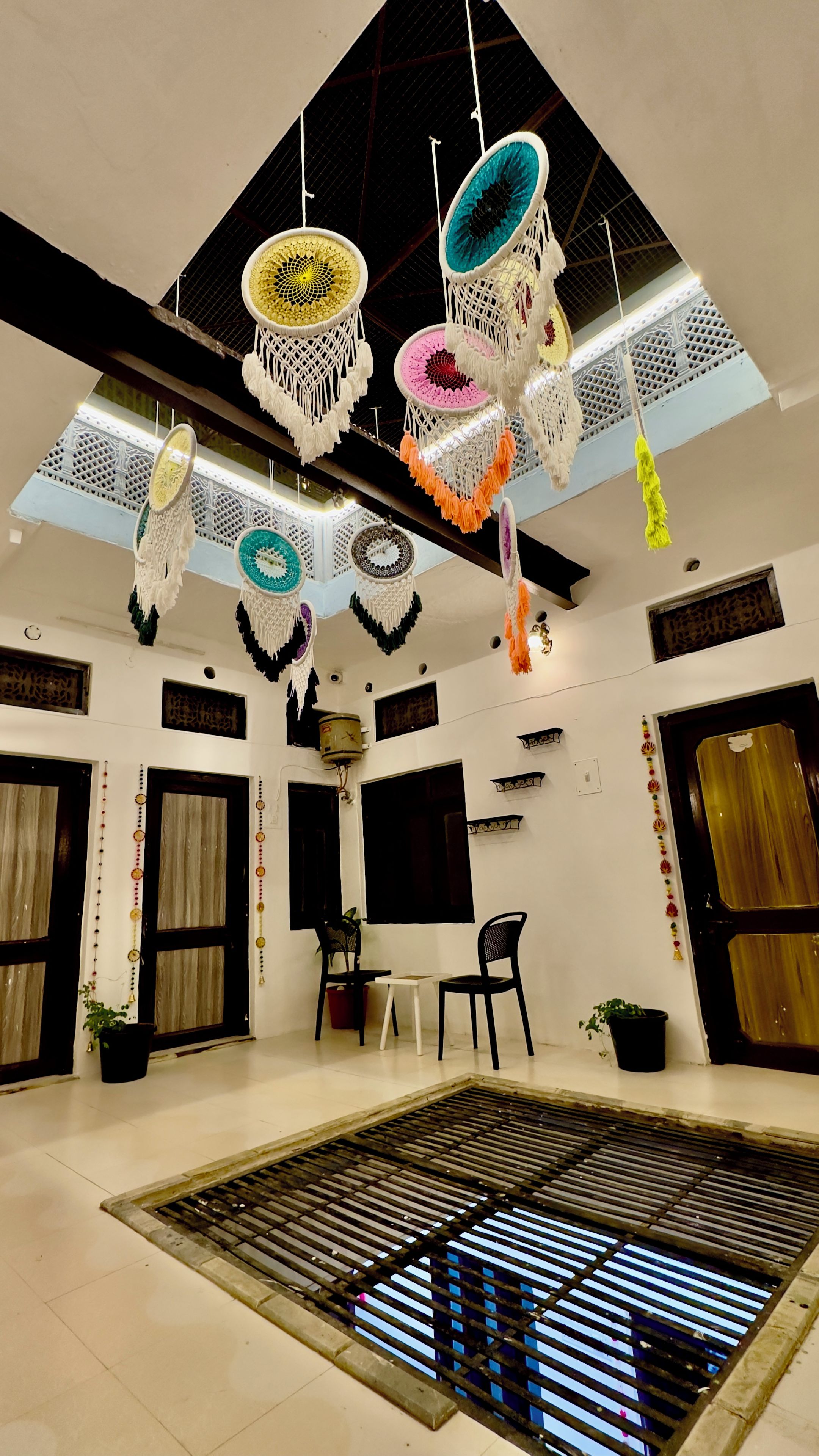Una stanza con soffitto alto, decorazioni in macramè appese al soffitto, un'area salotto centrale con tavolo e sedie, e un'ampia finestra con vista.
