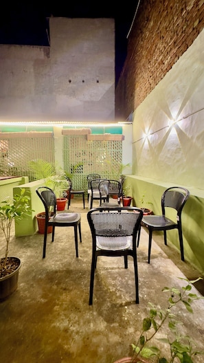 An outdoor seating area with chairs and tables, surrounded by potted plants and a green fence. - Hotel Hermosa Pushkar (Pushkar)