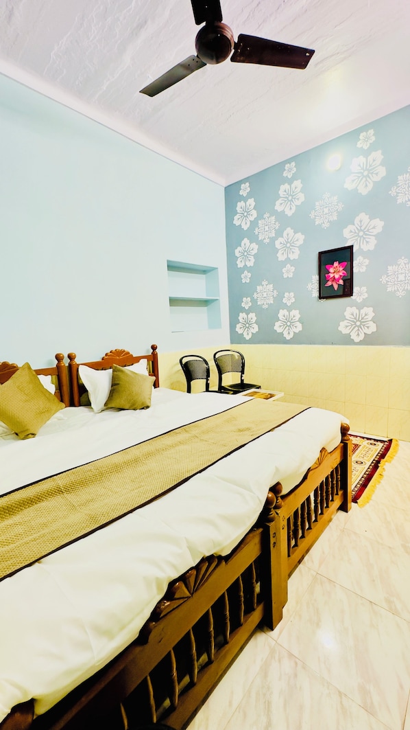 A bedroom with a bed, two chairs, a ceiling fan, and a wall with floral wallpaper. - Hotel Hermosa Pushkar (Pushkar)