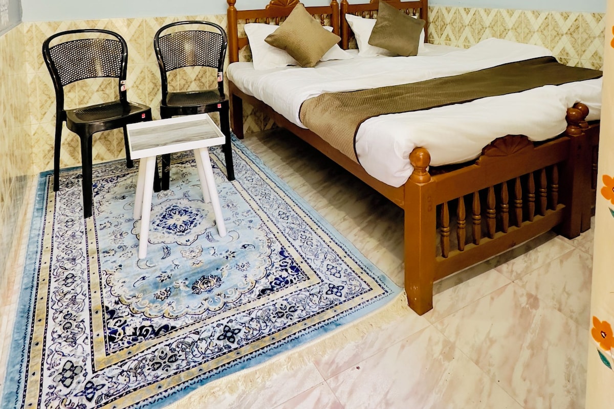 A bedroom with a bed, two chairs, a ceiling fan, and a patterned rug.