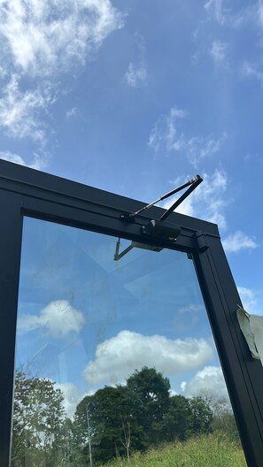 A window with a wiper mechanism, clear sky, and reflections of trees and clouds. - Pachamama pyramid 3 (La cruz)