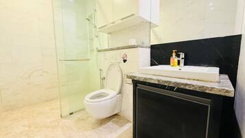 A modern bathroom with a glass shower enclosure, a toilet, and a sink with a marble countertop.