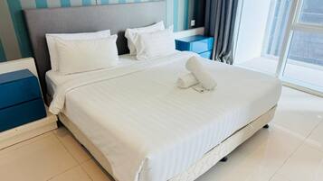 A neatly made bed with white linens, a grey headboard, and a blue bedside table with a blue box.