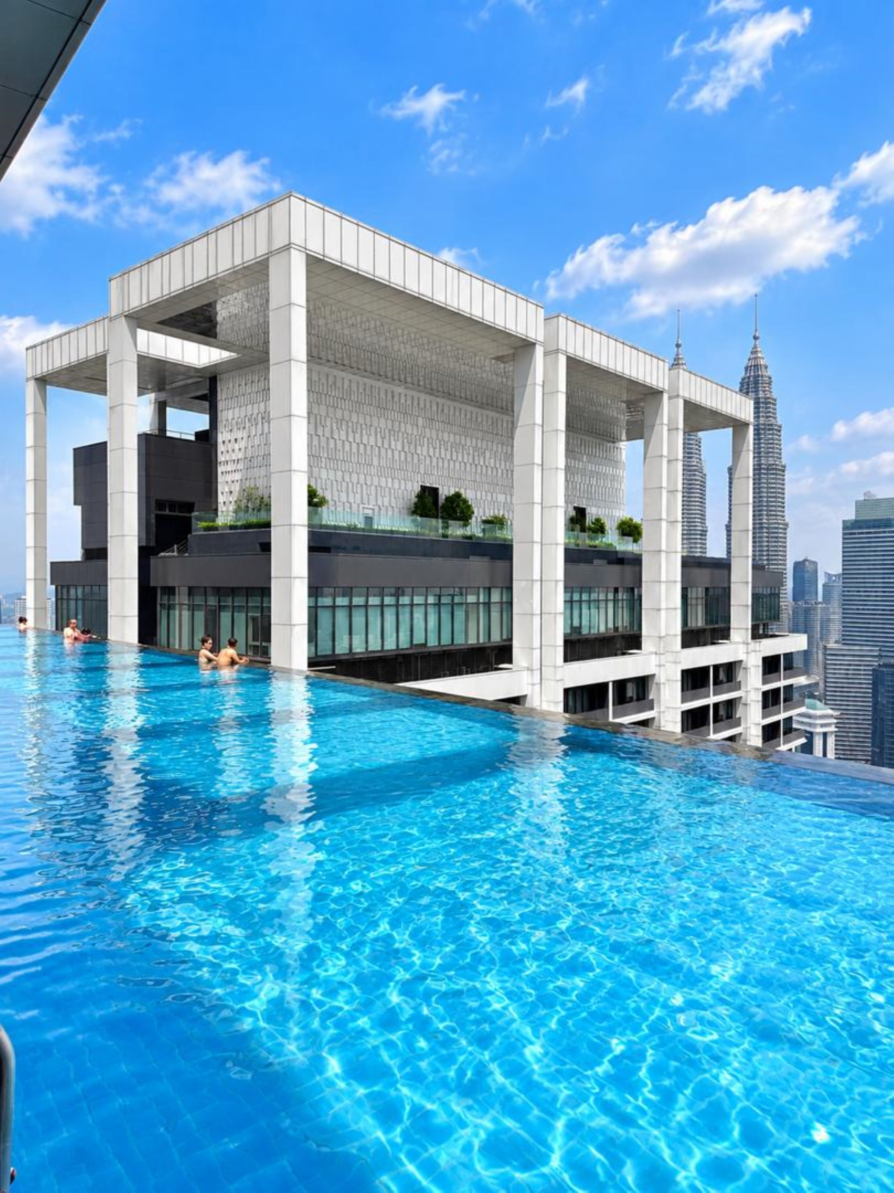 Un edificio moderno con piscina infinita en la azotea, rodeado de rascacielos.