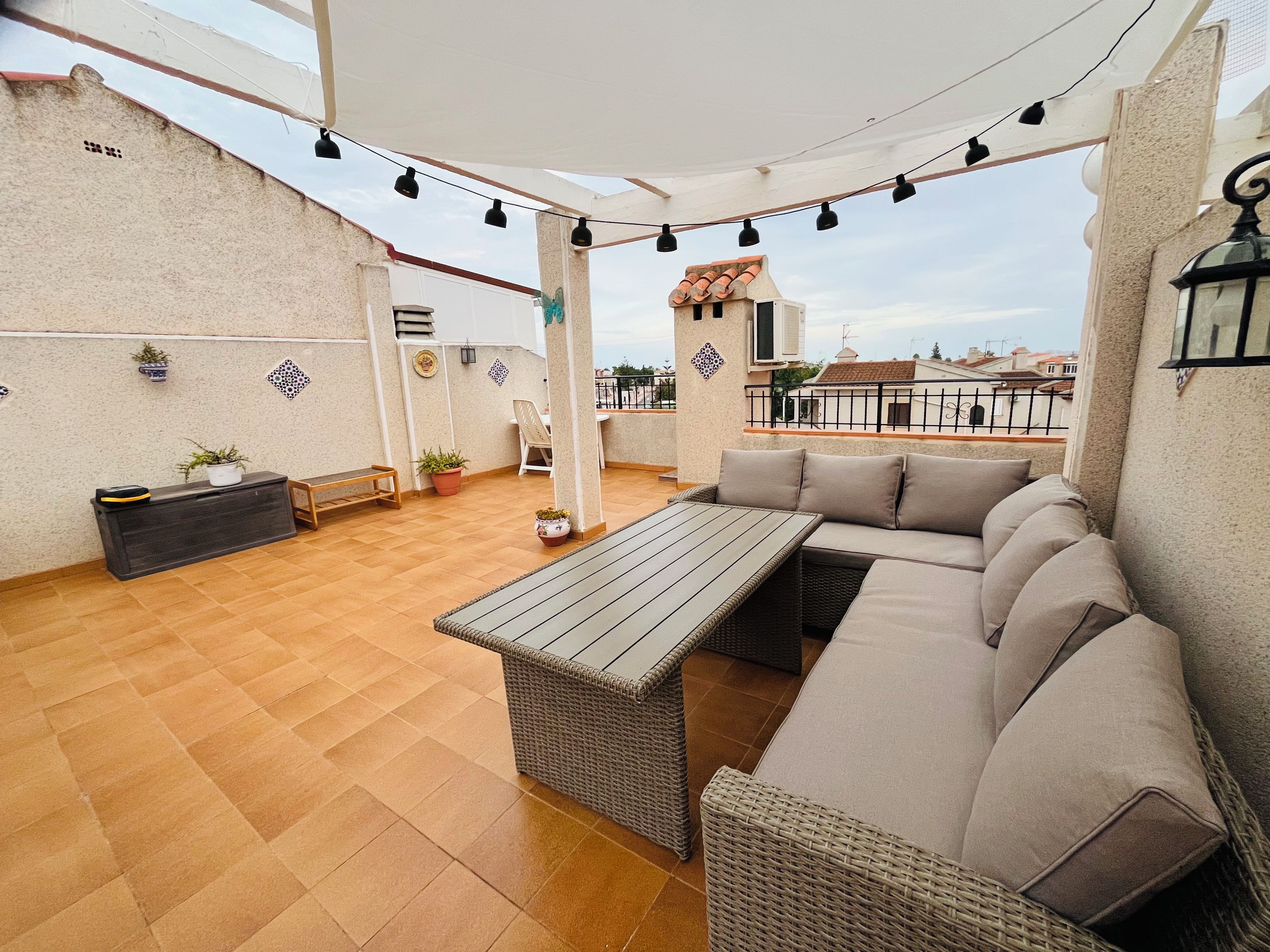 An outdoor patio with a sofa, table, and potted plants.
