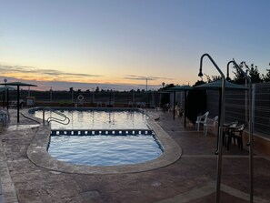 Ein Schwimmbad mit einer umlaufenden Sonnenterrasse, Liegestühlen und Blick auf den Sonnenuntergang.