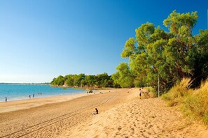 Ein Sandstrand mit Menschen, Bäumen und blauem Himmel.