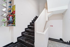 A staircase with black marble steps leading to a landing, a fire extinguisher mounted on the wall, and a fire exit sign.