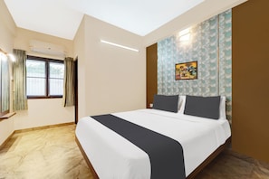 Una habitación de hotel con cama, ventana con cortinas, pared con papel tapiz estampado y un cuadro.