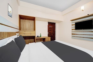 A modern hotel room with a bed, a wooden wardrobe, a desk, a television, and a door. - Super Hotel O Vilankurichi (Coimbatore)