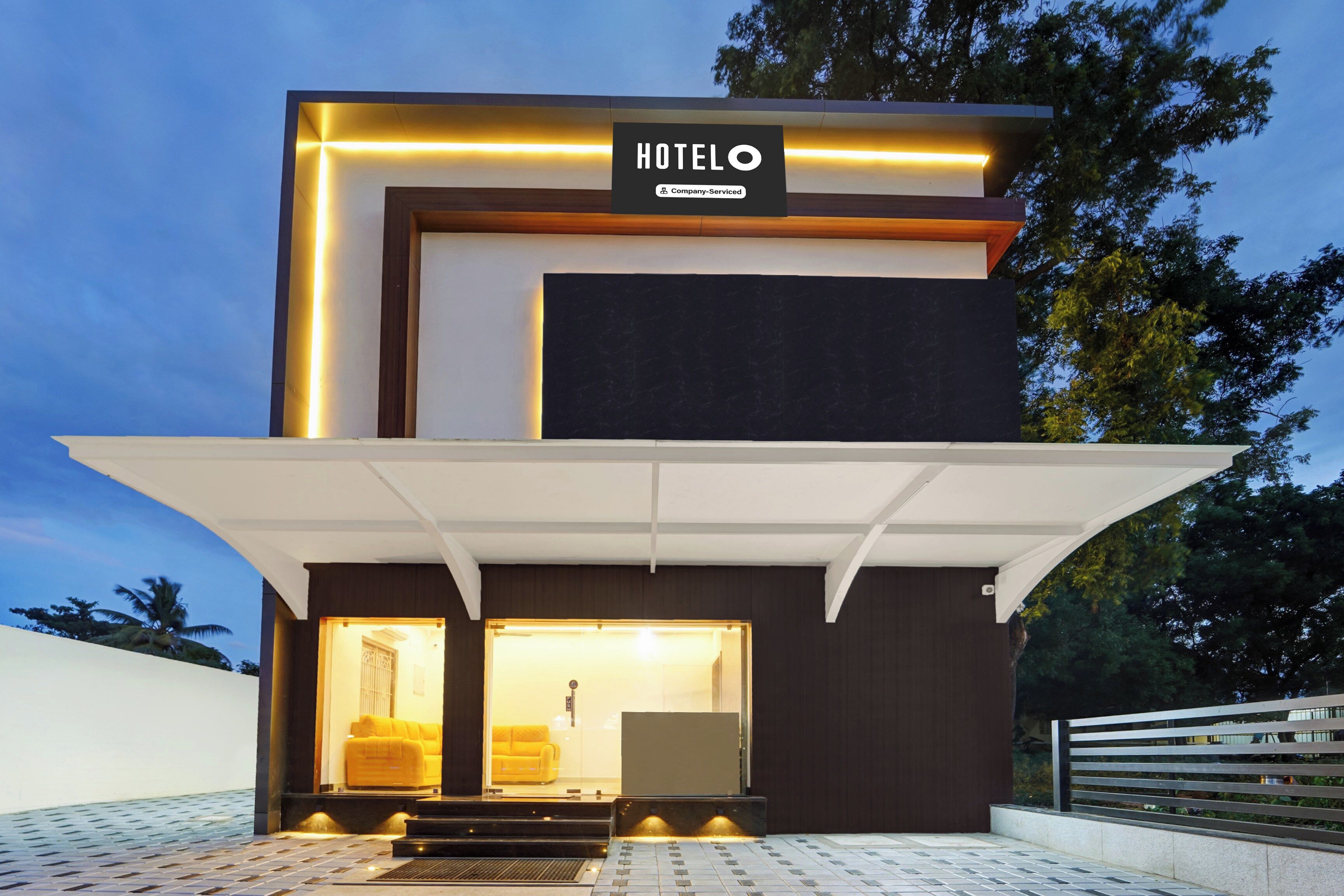 Un hotel moderno con un letrero llamativo, un acceso cubierto y un interior visible que incluye un sofá.