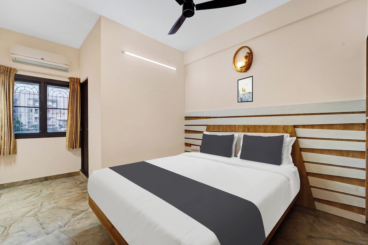 Habitación de hotel con cama, ventilador de techo, ventana con cortinas y lámpara fijada a la pared.