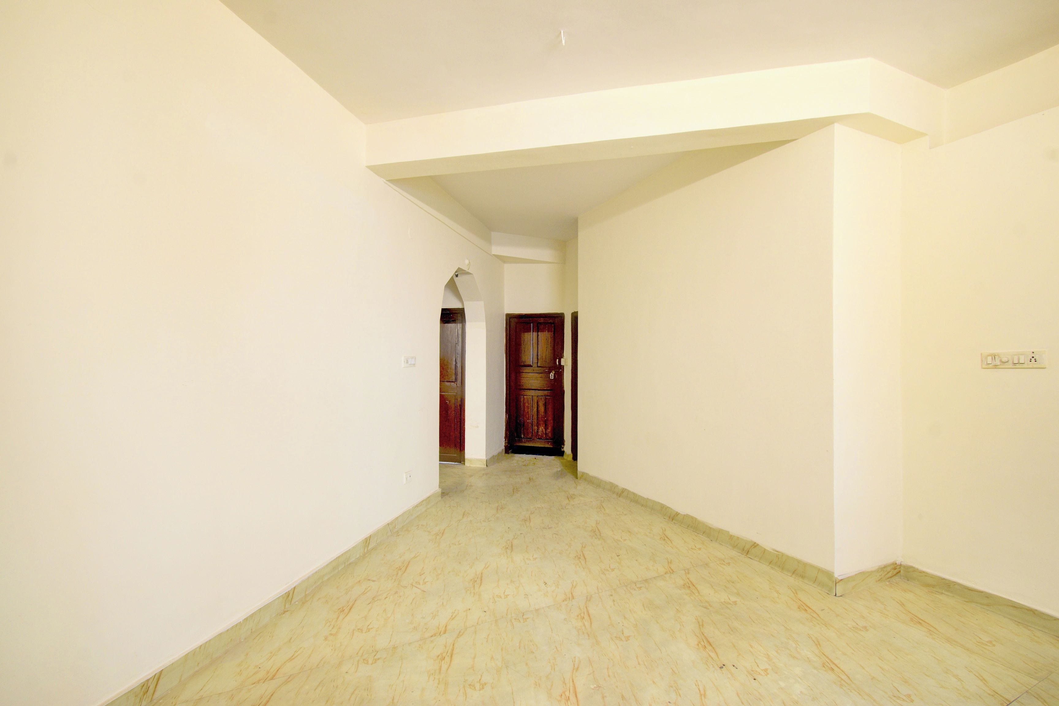 A corridor with white walls and a marble floor leading to a wooden door.