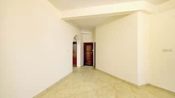 Un couloir aux murs blancs et au sol en marbre, qui mène à une porte en bois.