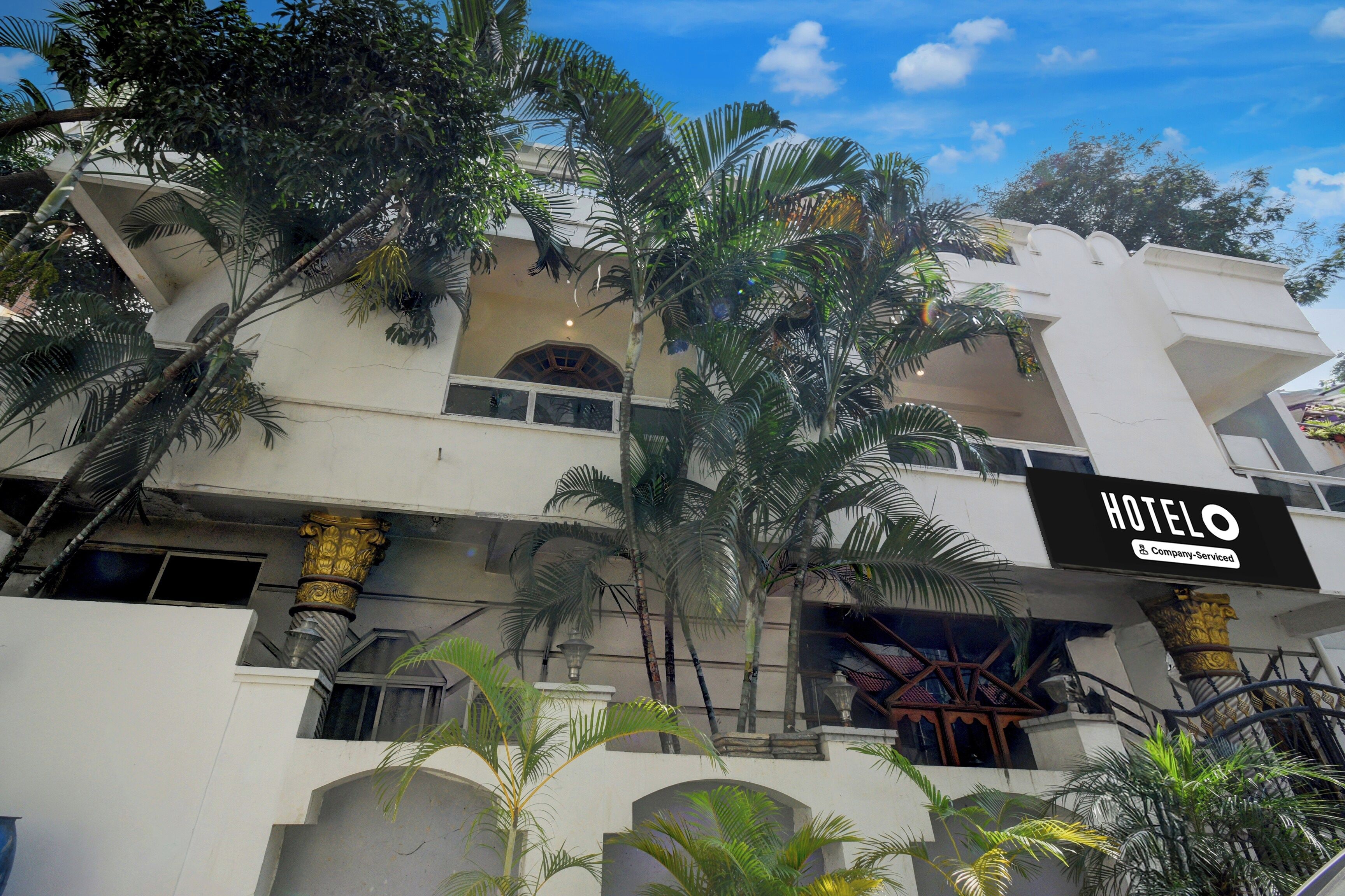 Un hotel con letrero, varios balcones y palmeras.