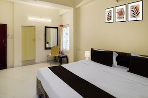 Quarto de hotel com uma cama grande, uma mesa com cadeira, um espelho e três quadros na parede.