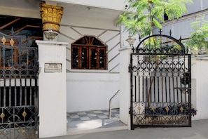A gated entrance with a metal gate and a wooden door, a white wall, and a staircase leading to a door with a glass panel.
