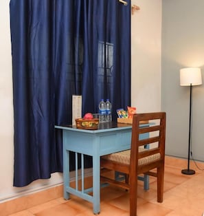 A room with a blue table and chair, a lamp, and a window with curtains. - Bens Inn Ashwem Beach (Ashvem)