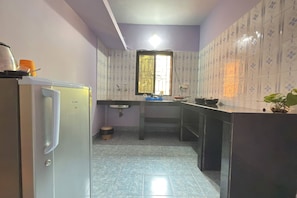 A compact kitchen with a refrigerator, sink, and a window with bars. - Bens Inn Ashwem Beach (Ashvem)