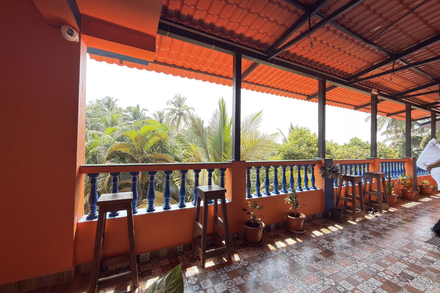 A covered balcony with a tiled floor, potted plants, and a view of palm trees.