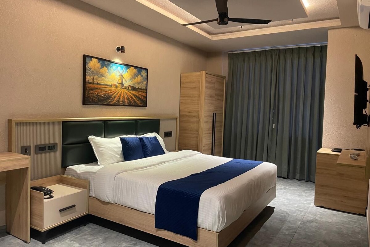 A hotel room with a bed, bedside table, wardrobe, and a painting on the wall.