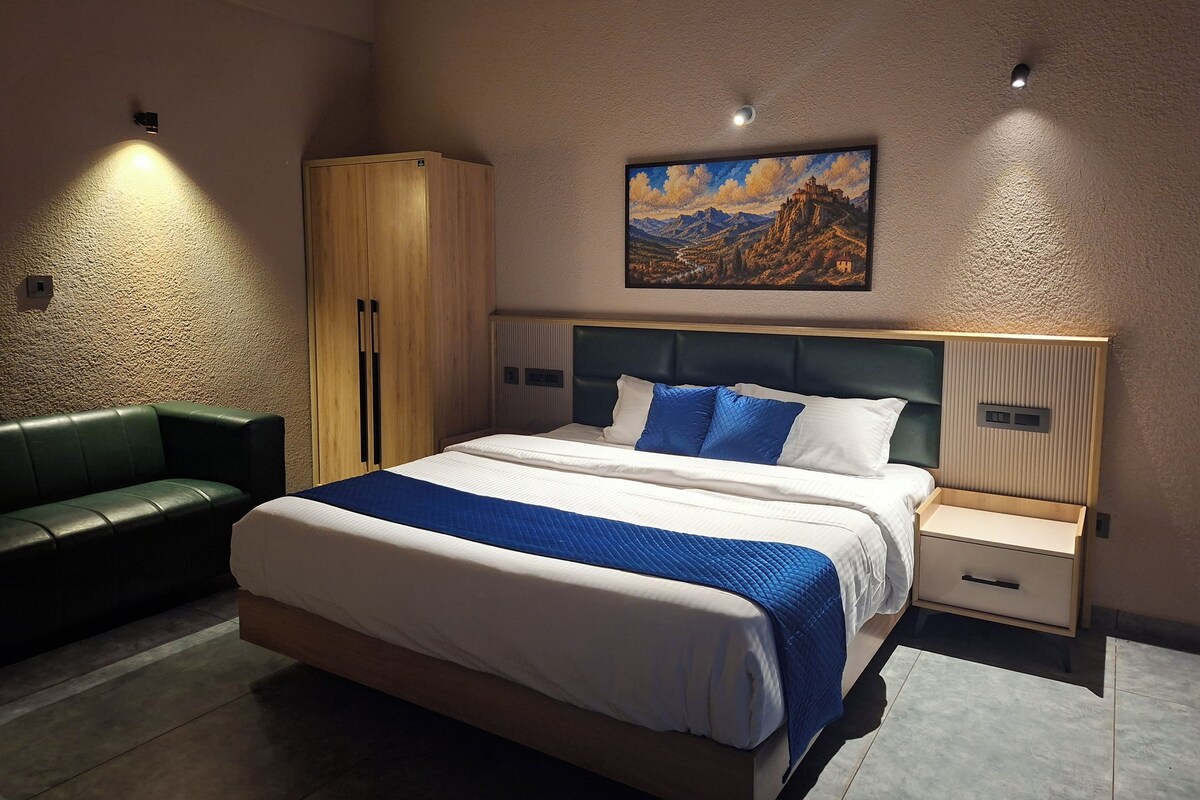 A modern bedroom with a bed, a green sofa, a wooden wardrobe, and a painting on the wall.