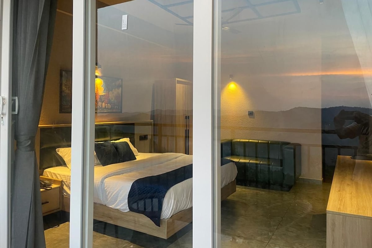 A bedroom with a bed, bedside table, and a view of a landscape through a glass door.