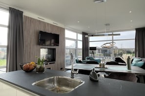 A modern kitchen with a large window, a flat-screen TV, and a dining area with a table and chairs. - Dream Chalet Olburgen (ND Olburgen)