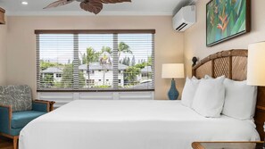 A hotel room with a large bed, a view of palm trees and houses, a ceiling fan, and a wall-mounted air conditioner. - Club Wyndham Bali Hai Villas - 2BR Presidential, Princeville Kauai (Princeville)