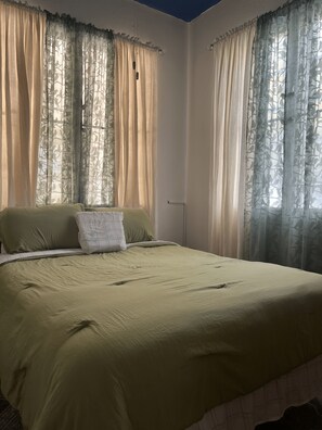 A bedroom with a bed, curtains, and a door. - Rehoboth Ginnah Manor - Rural Chalet w/ Wifi & AC (Sand Hill)