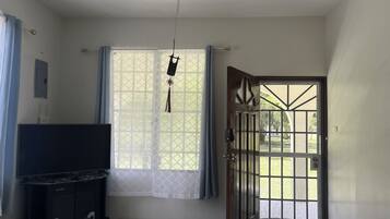 A room with a television on a cabinet, a window with curtains, and a door leading outside.