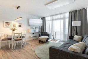 A modern living room with a sofa, chairs, a coffee table, and a TV mounted on the wall. - Sea la Vie holiday apartment (Fehmarn Burgtiefe)