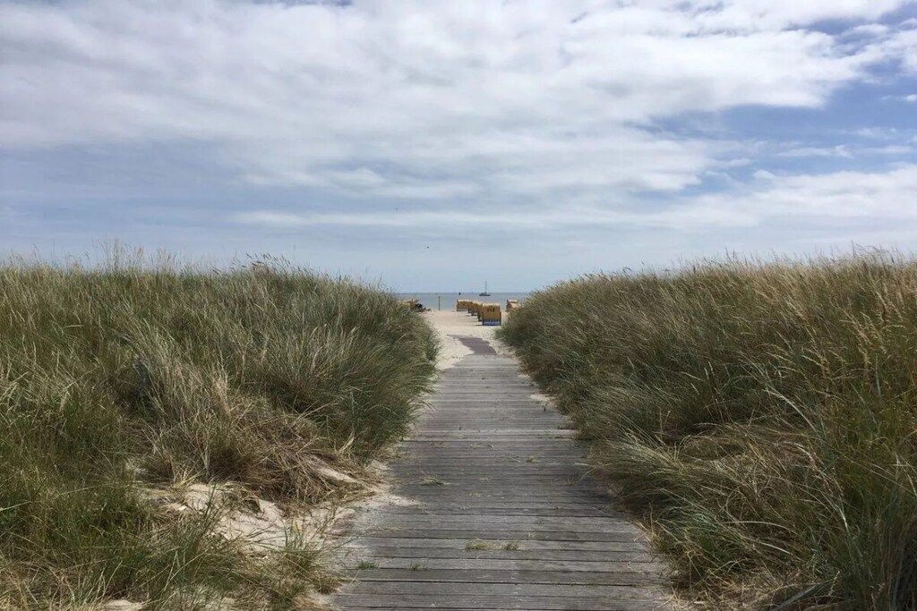 A wooden boardwalk leading to a beach with sand and grassy dunes on either side.