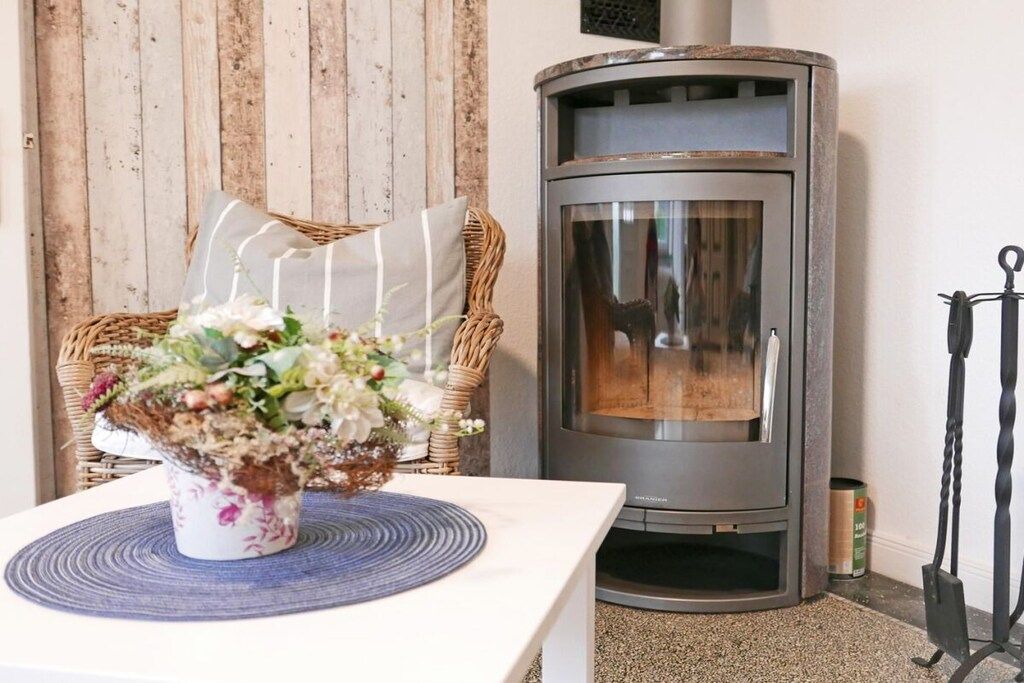 A corner room with a fireplace, a wicker chair, and a table with a floral arrangement.