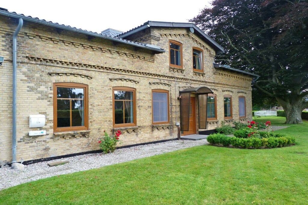 Ein zweistöckiges Steinhaus mit einer symmetrischen Fassade, großen Fenstern und einem kleinen Gartenbereich mit roten Blumen.