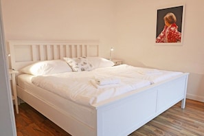 Ein weißes Bett mit Kopfteil, Nachttisch und einem Wandbild.