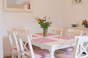A dining area with a white table, six white chairs, pink placemats, and a vase with flowers. - Holiday apartment with 1 bedroom (Kappeln)
