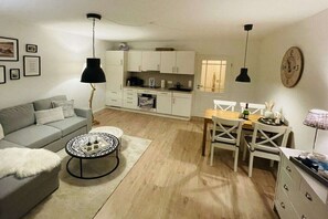 A compact living space with a sofa, coffee table, dining table with chairs, a kitchen area, and pendant lighting. - Beach castle “White” (Grömitz)