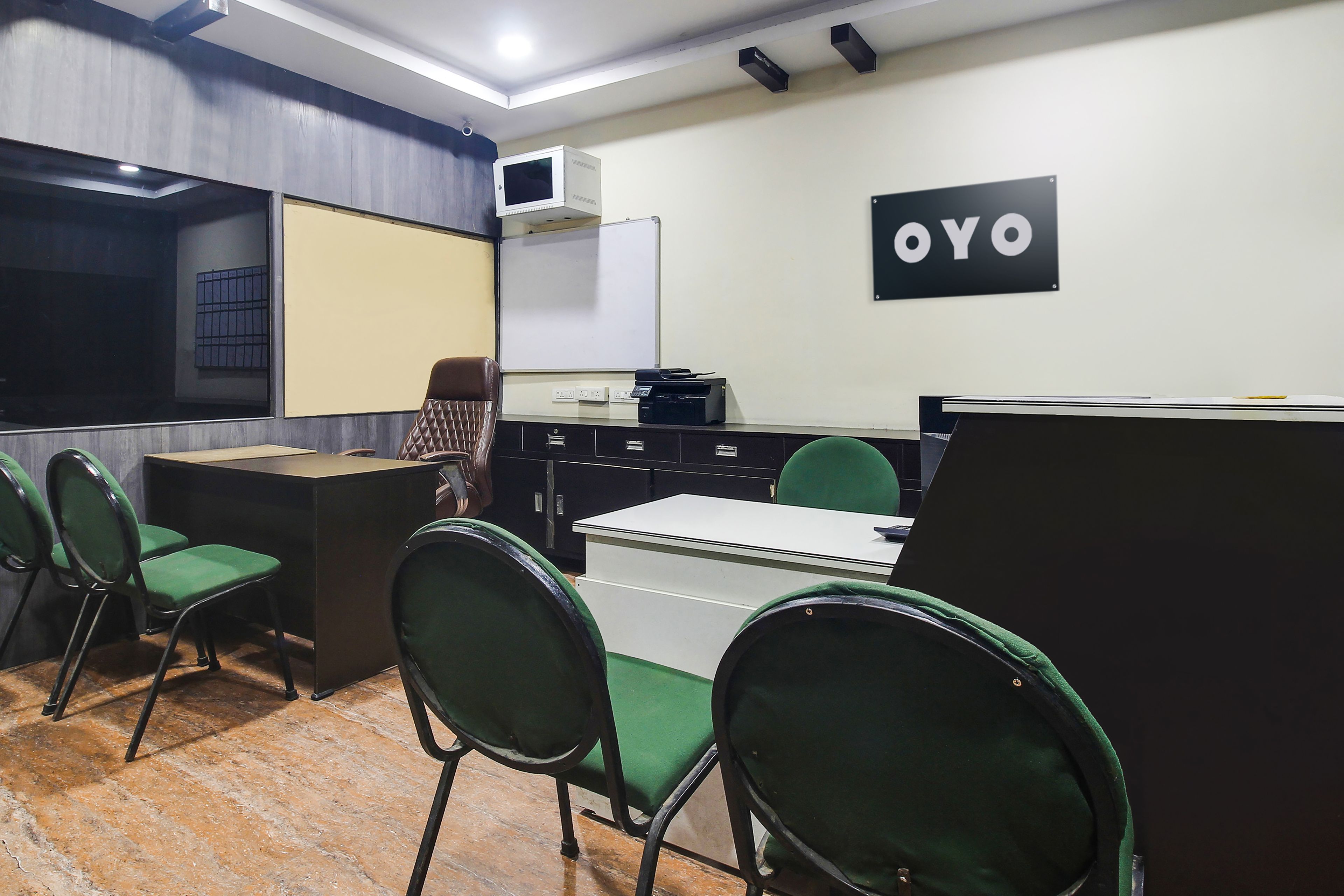 A conference room with a whiteboard, a blackboard, and a sign that reads 'OYO'. There are green chairs and a desk with a computer.